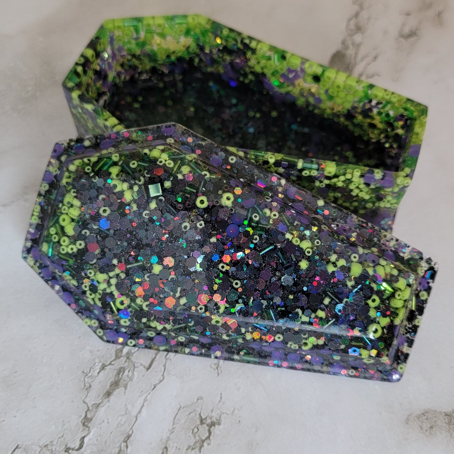 Coffin shaped epoxy resin trinket box, mixture of black chunky holographic glitter, various lime green beads and purple rhinestone glitters.