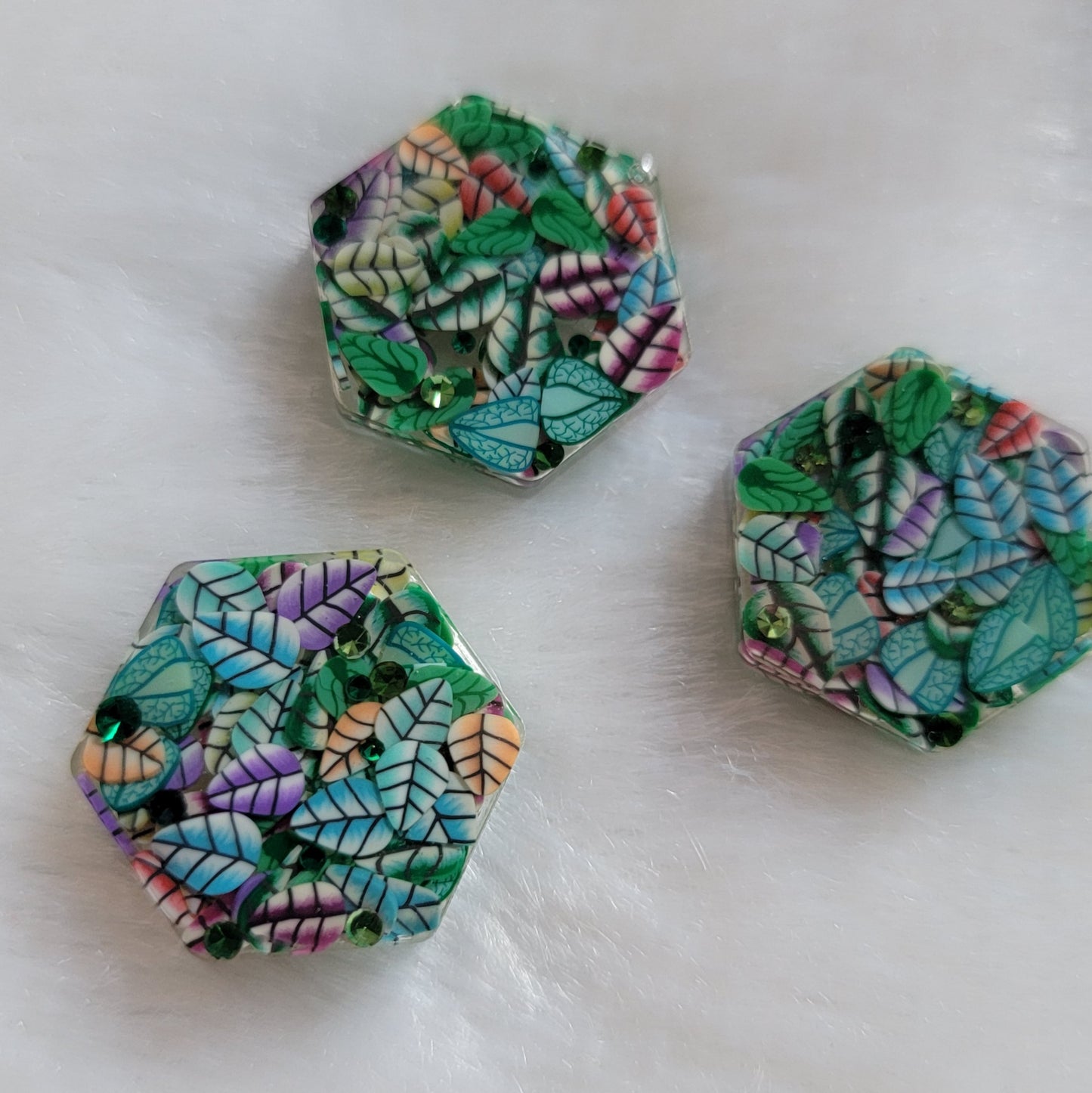 Three mini hexagon epoxy resin pieces, made with mixed polymer clay leaves and green rhinestones.