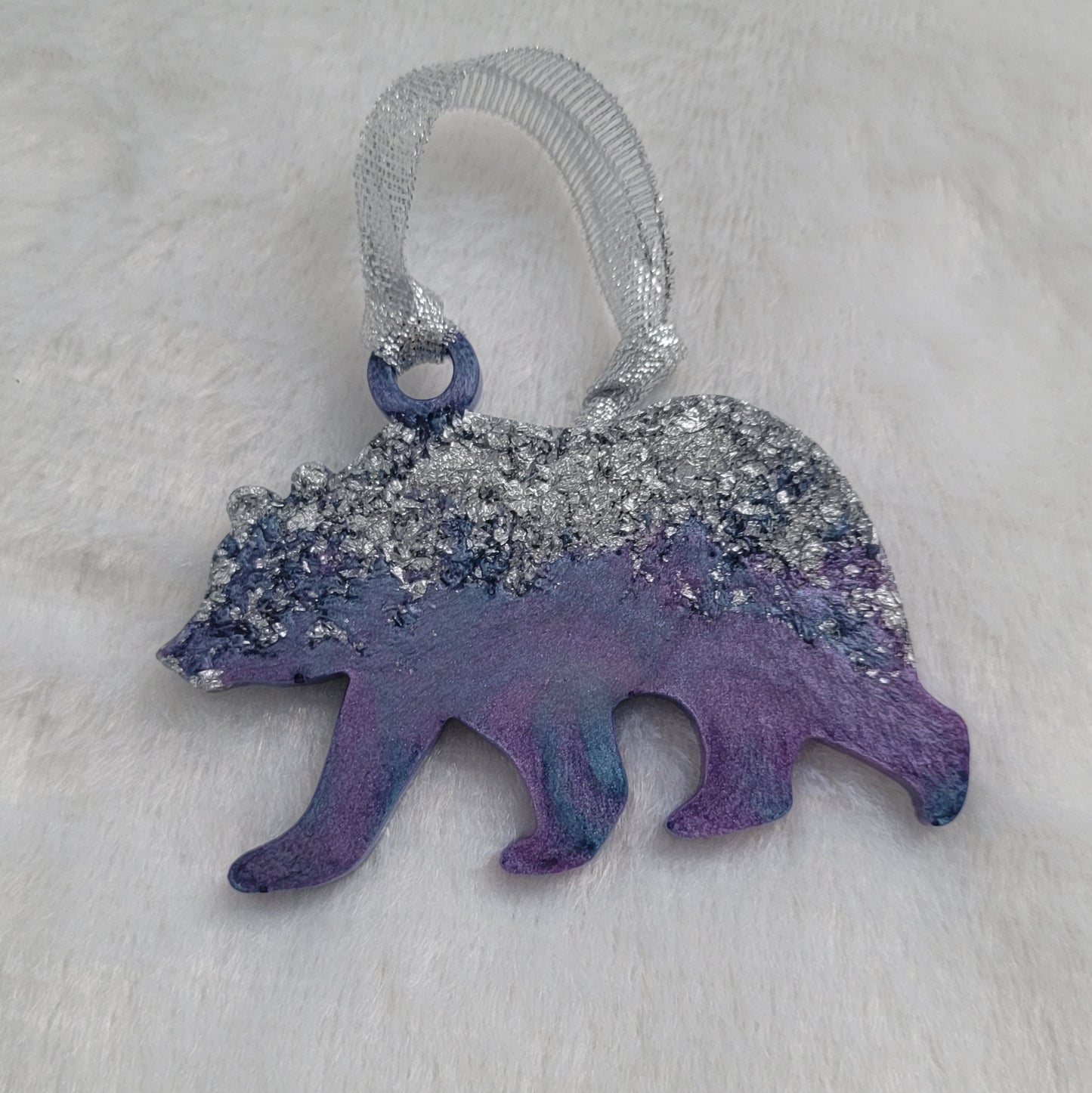 Bear shaped epoxy resin ornament, made with silver foil flakes with lavender and light blue swirls and a sparkling silver ribbon attached.