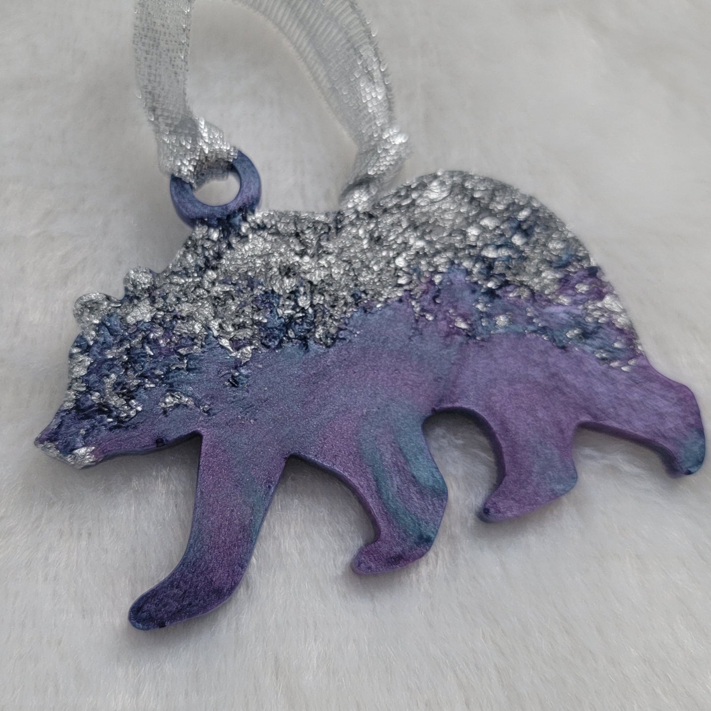 Bear shaped epoxy resin ornament, made with silver foil flakes with lavender and light blue swirls and a sparkling silver ribbon attached.