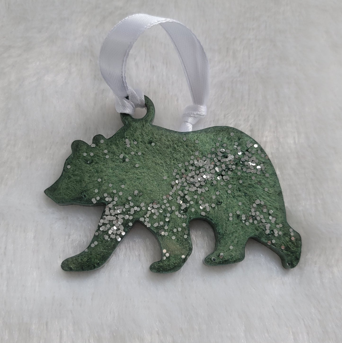 Bear shaped epoxy resin ornament, made with deep green mica pigment, bright silver glitter and a white ribbon attached.
