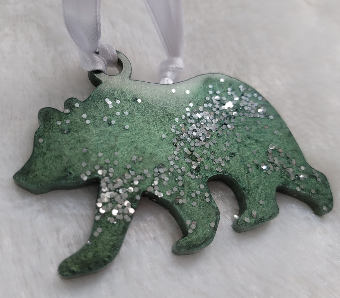 Bear shaped epoxy resin ornament, made with deep green mica pigment, bright silver glitter and a white ribbon attached.