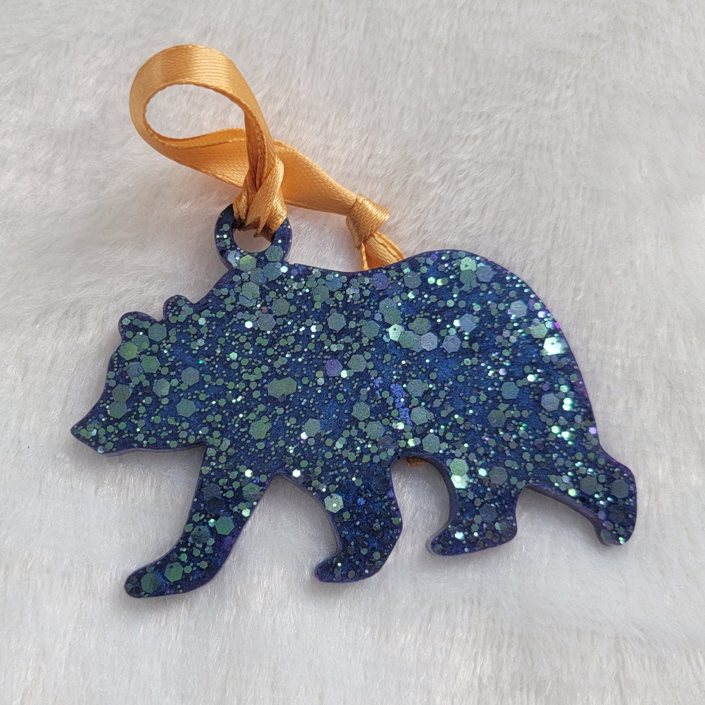 Bear shaped epoxy resin ornament, made with purple and aqua blue holographic glitter and a gold ribbon attached.