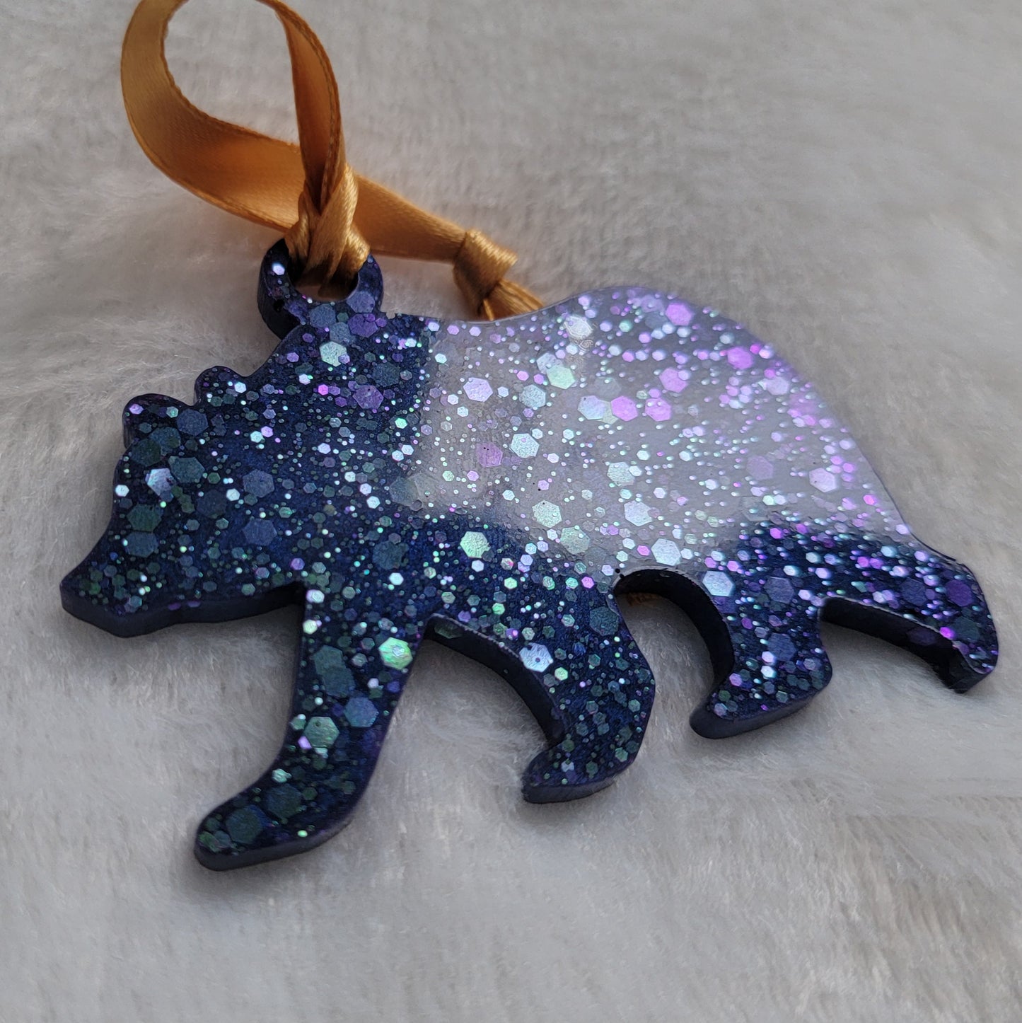 Bear shaped epoxy resin ornament, made with purple and aqua blue holographic glitter and a gold ribbon attached.