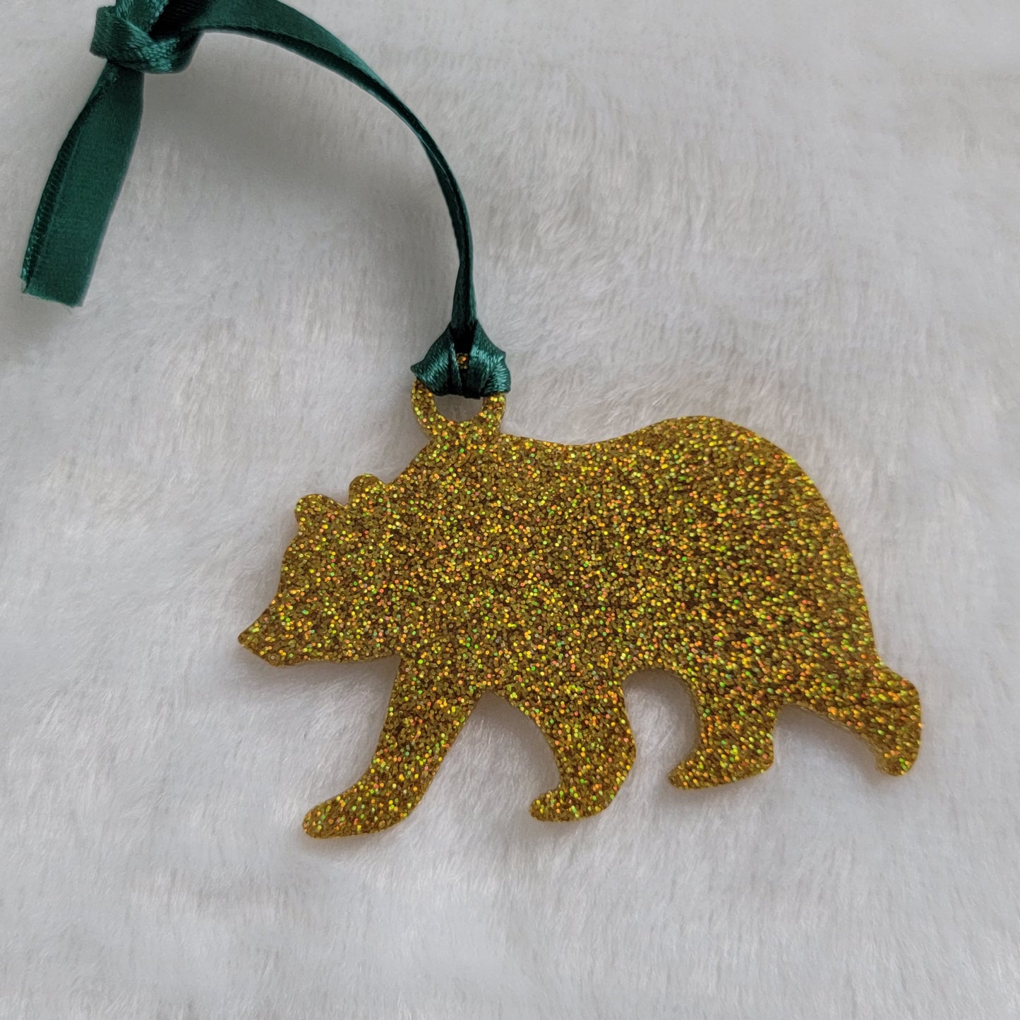 Bear shaped epoxy resin ornament, made with gold holographic glitter and a dark green ribbon attached.