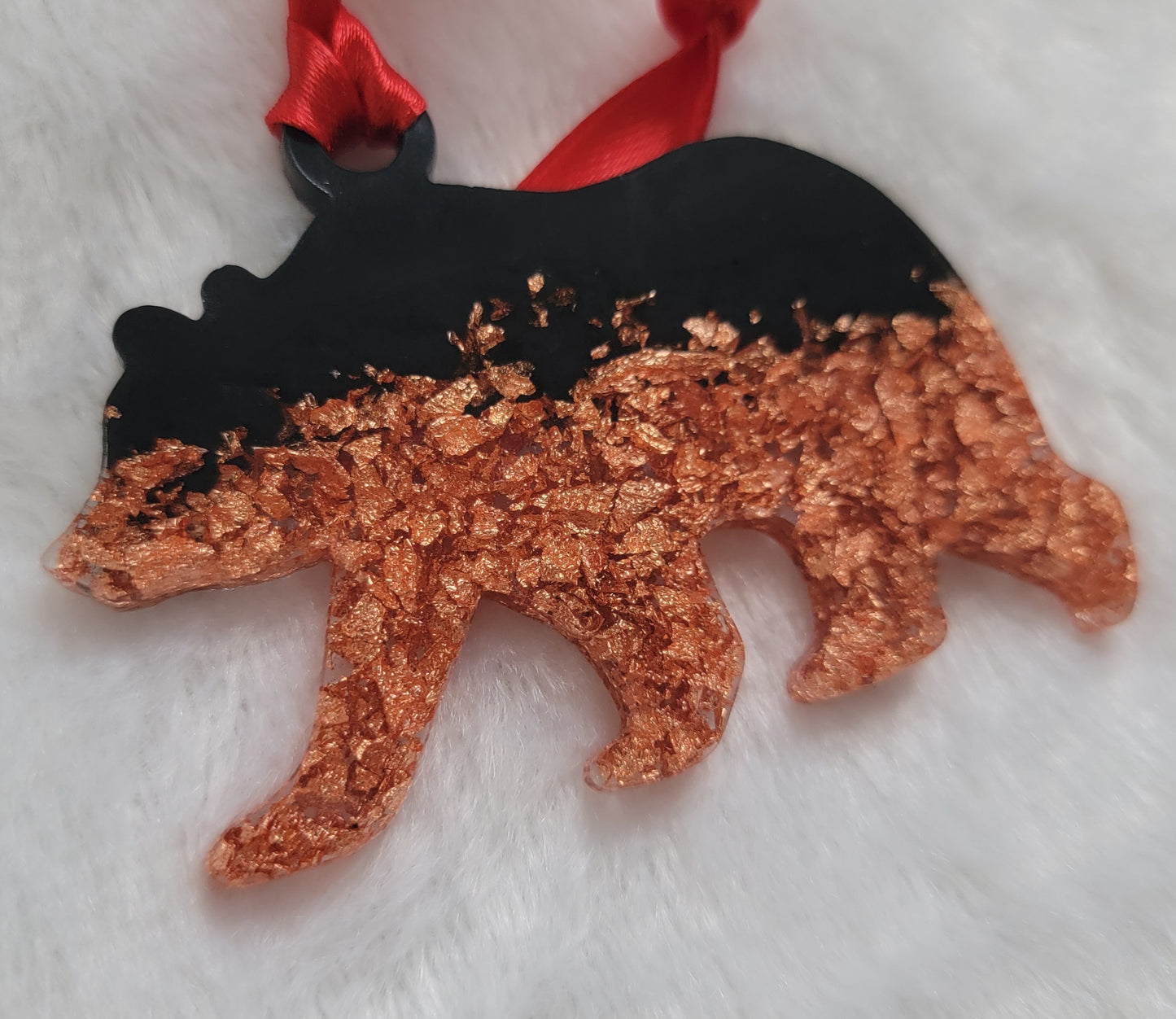 Bear shaped epoxy resin ornament, made with copper foil flakes and black pigment and a bright red ribbon attached.
