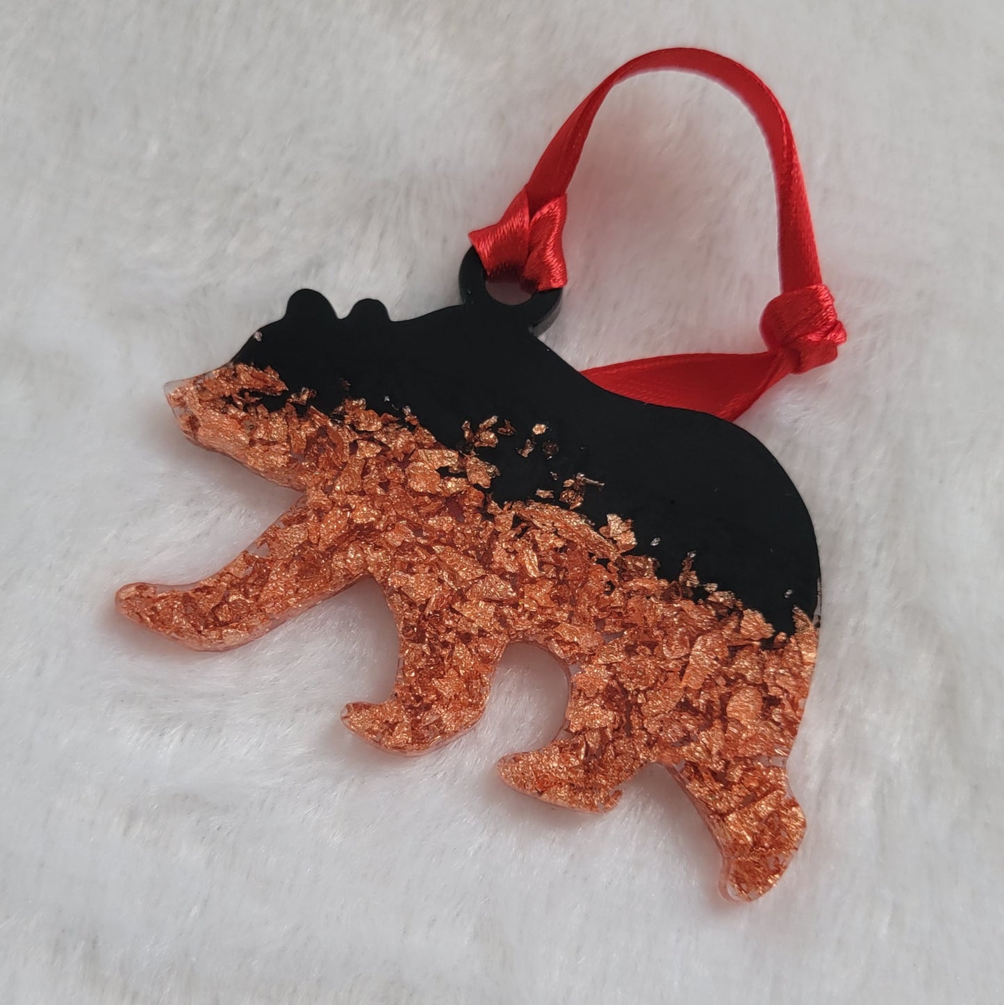 Bear shaped epoxy resin ornament, made with copper foil flakes and black pigment and a bright red ribbon attached.