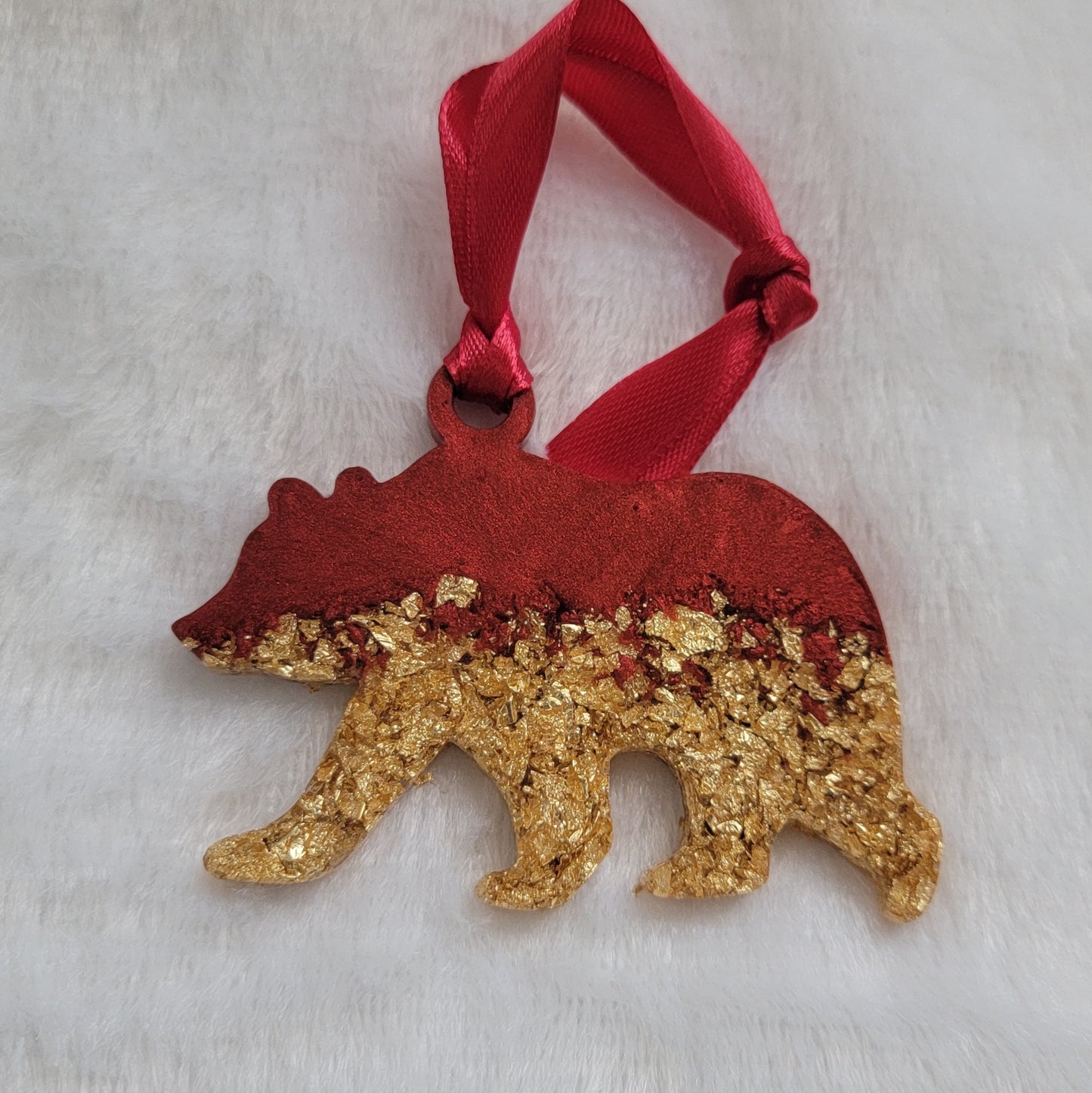 Bear shaped epoxy resin ornament, made with gold foil flakes and cherry red pigment and a red ribbon attached.