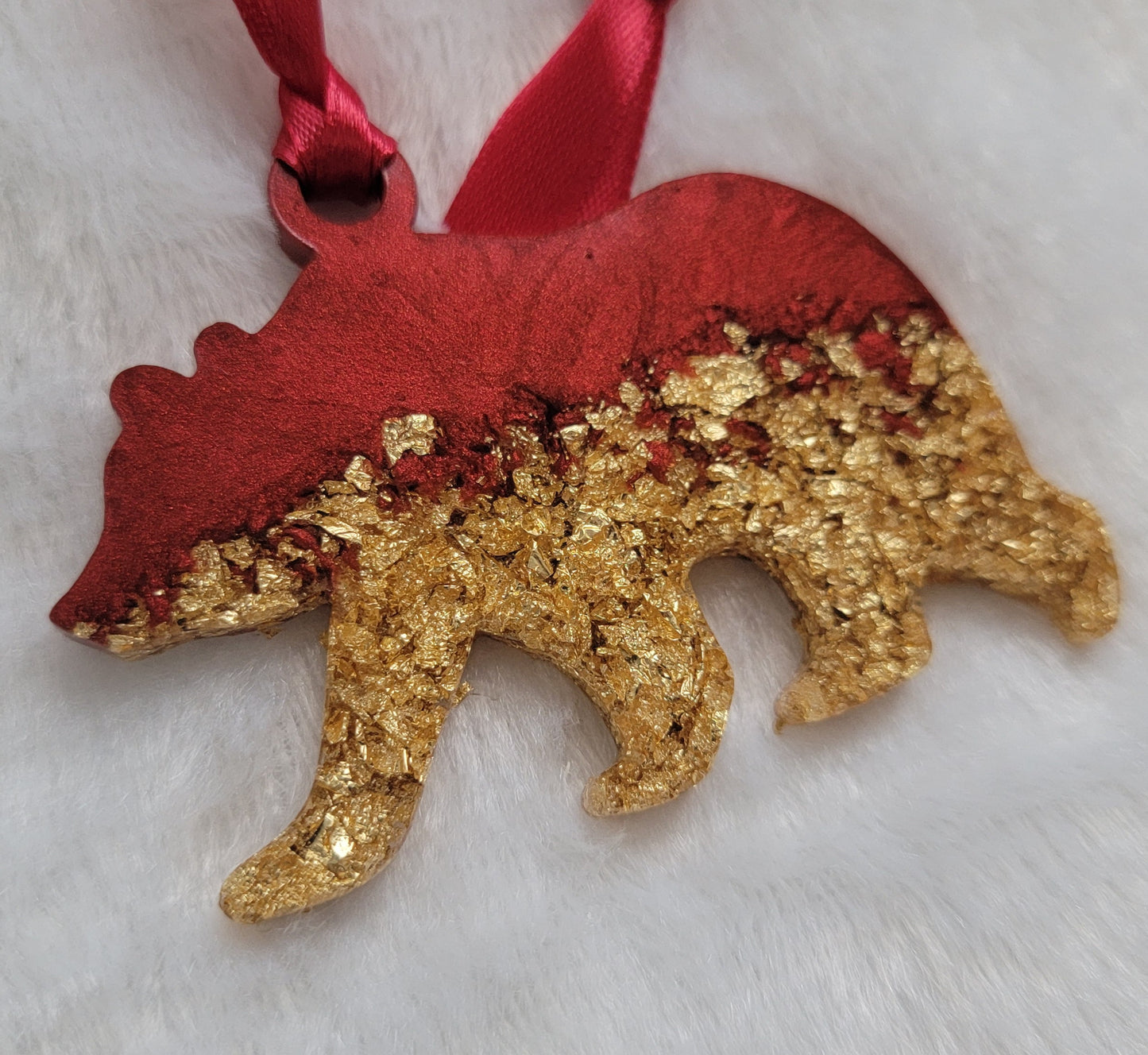 Bear shaped epoxy resin ornament, made with gold foil flakes and cherry red pigment and a red ribbon attached.