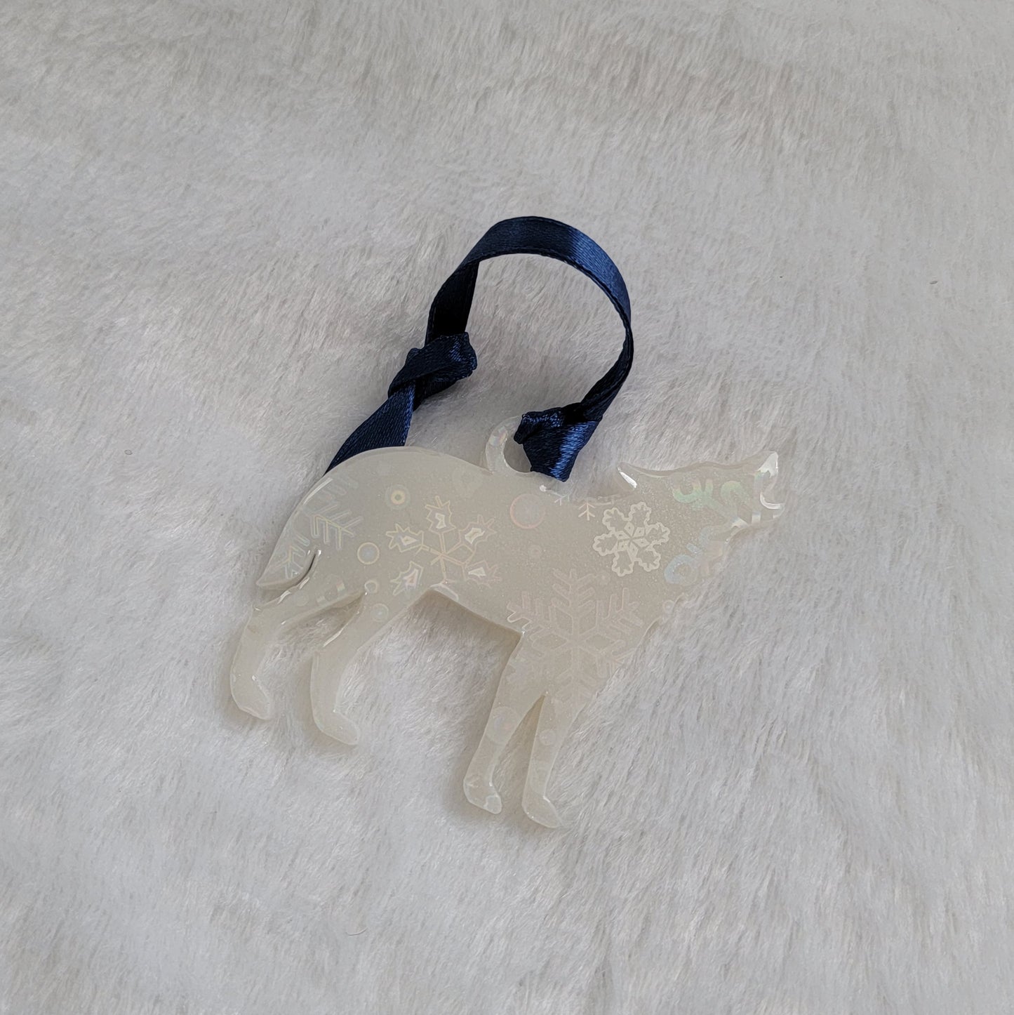 Wolf shaped epoxy resin ornament, made with white pigment with a holographic snowflake print vinyl covering the entire piece and a dark blue ribbon attached.
