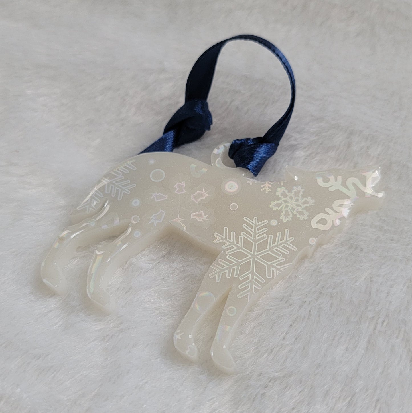 Wolf shaped epoxy resin ornament, made with white pigment with a holographic snowflake print vinyl covering the entire piece and a dark blue ribbon attached.