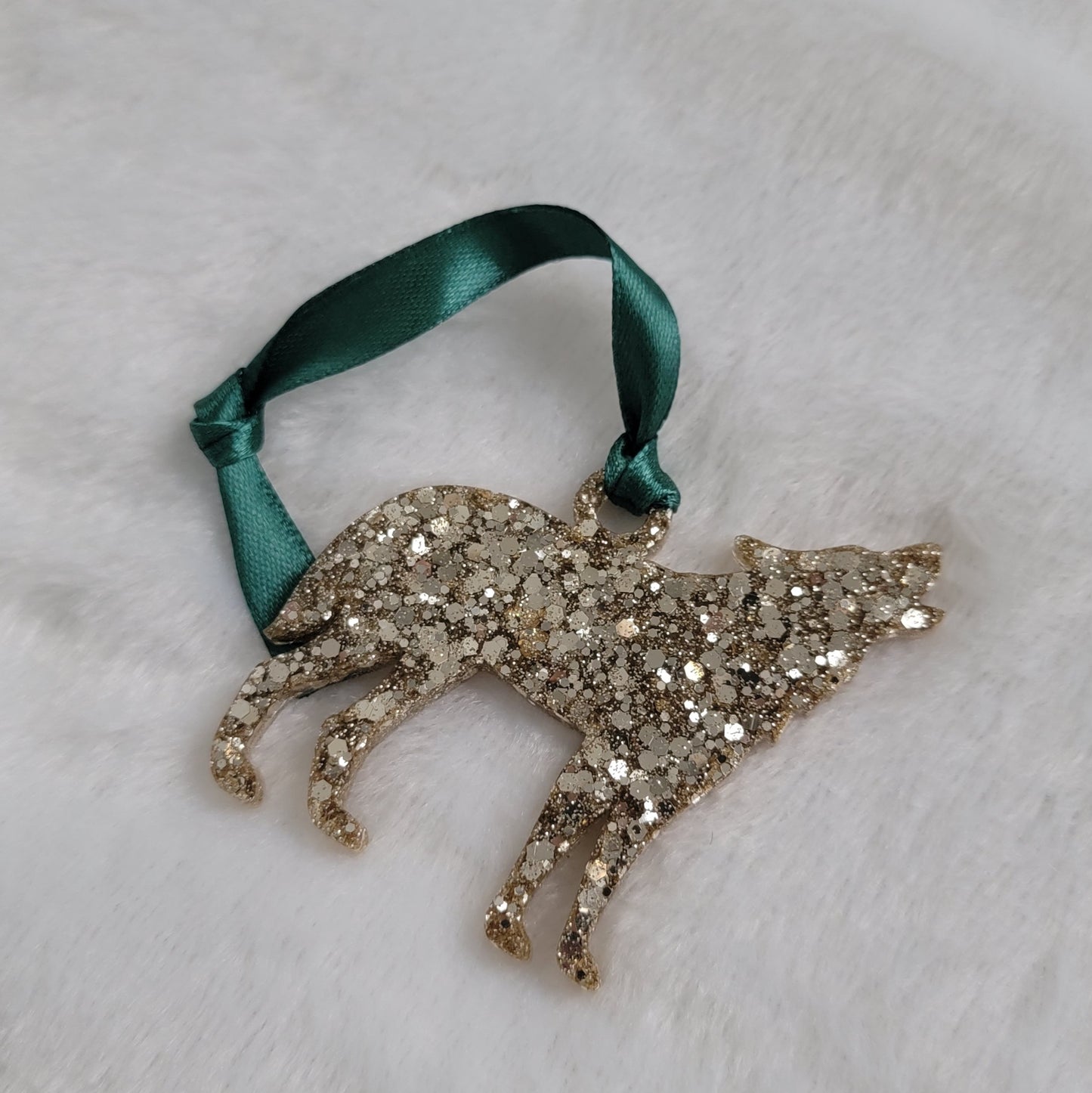 Wolf shaped epoxy resin ornament, made with warm silver glitter and a dark green ribbon attached.