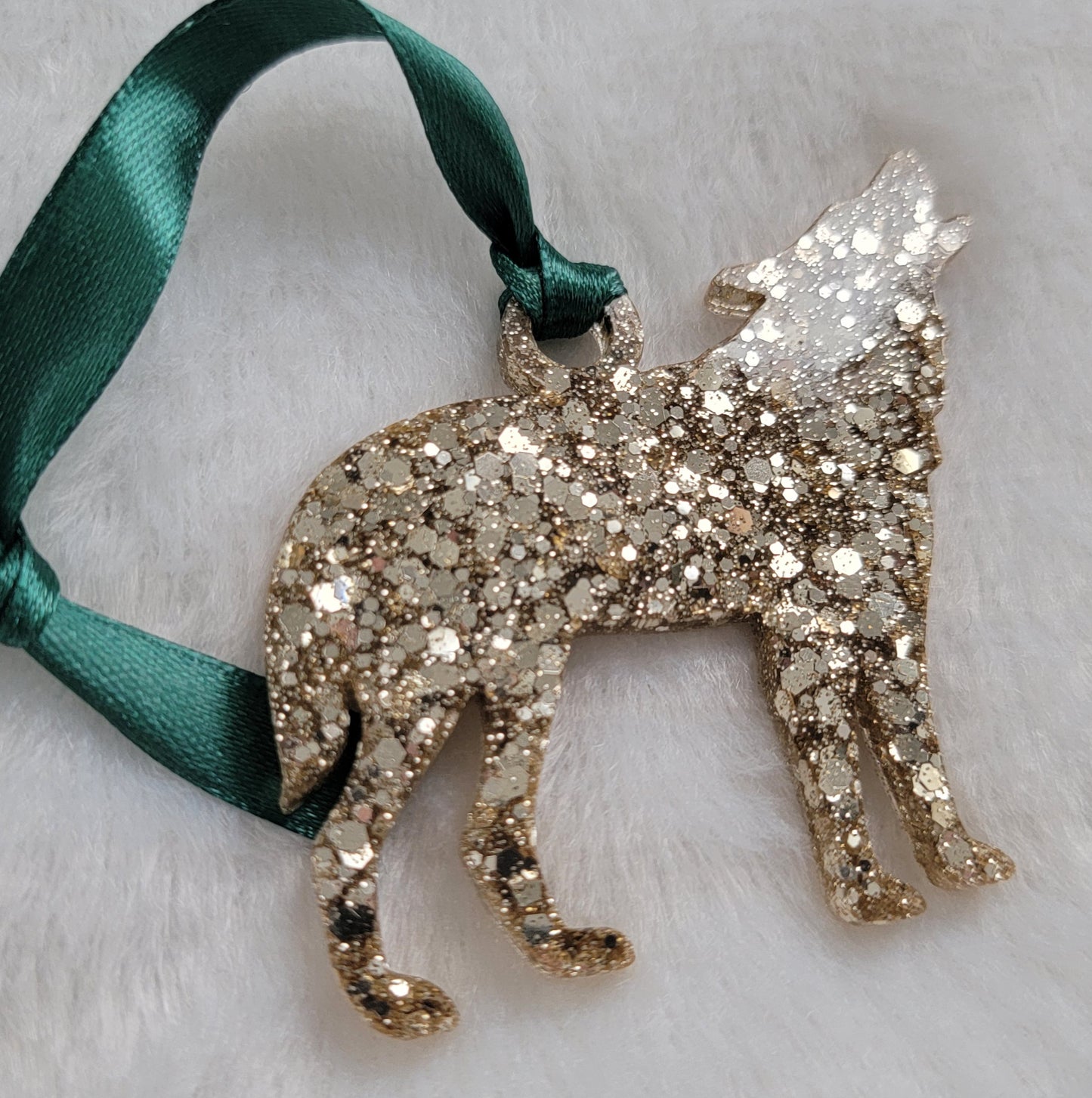 Wolf shaped epoxy resin ornament, made with warm silver glitter and a dark green ribbon attached.