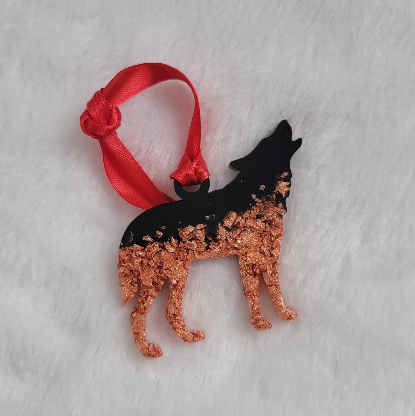 Wolf shaped epoxy resin ornament, made with copper foil flakes and black pigment and a bright red ribbon attached.