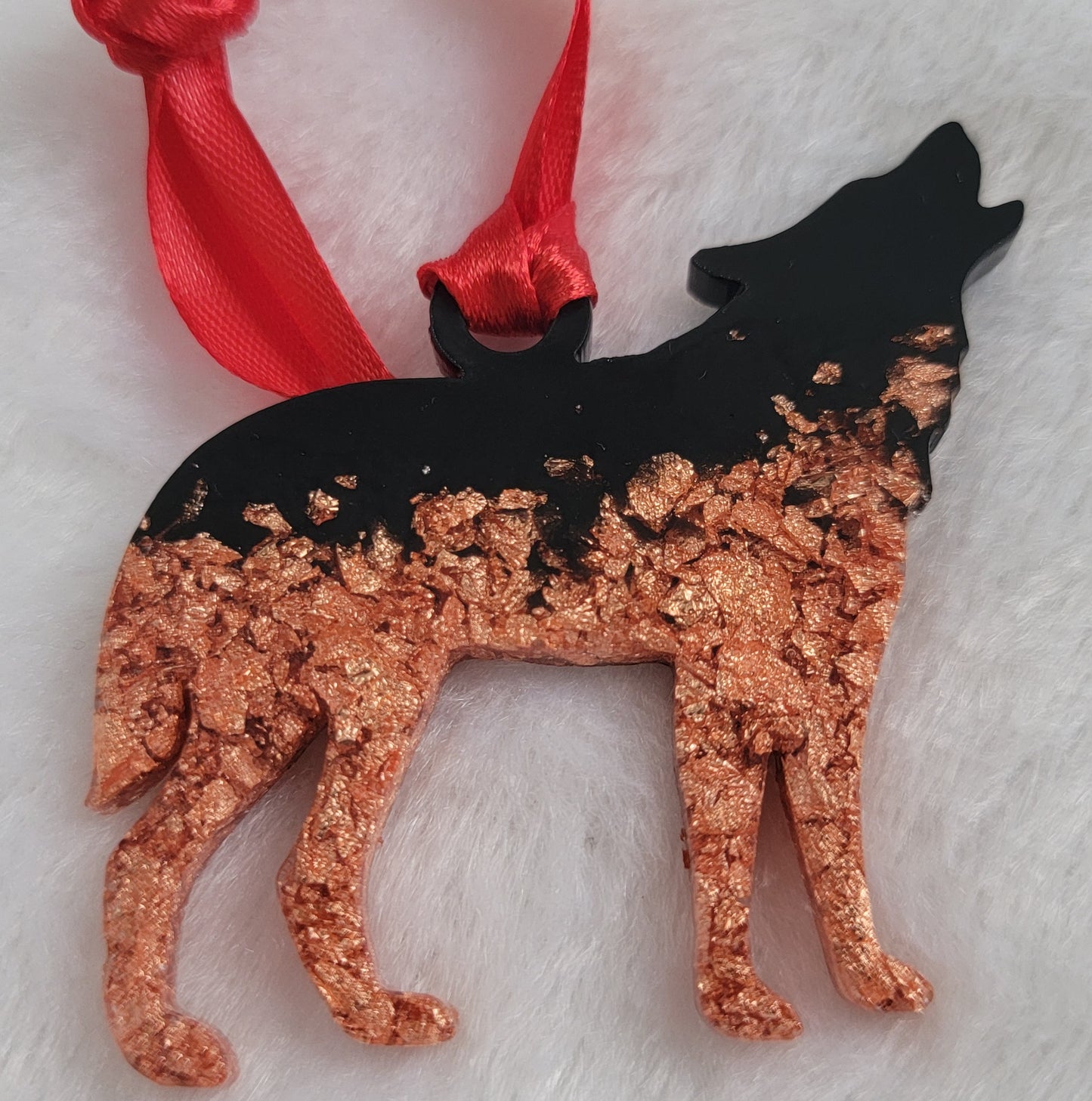 Wolf shaped epoxy resin ornament, made with copper foil flakes and black pigment and a bright red ribbon attached.