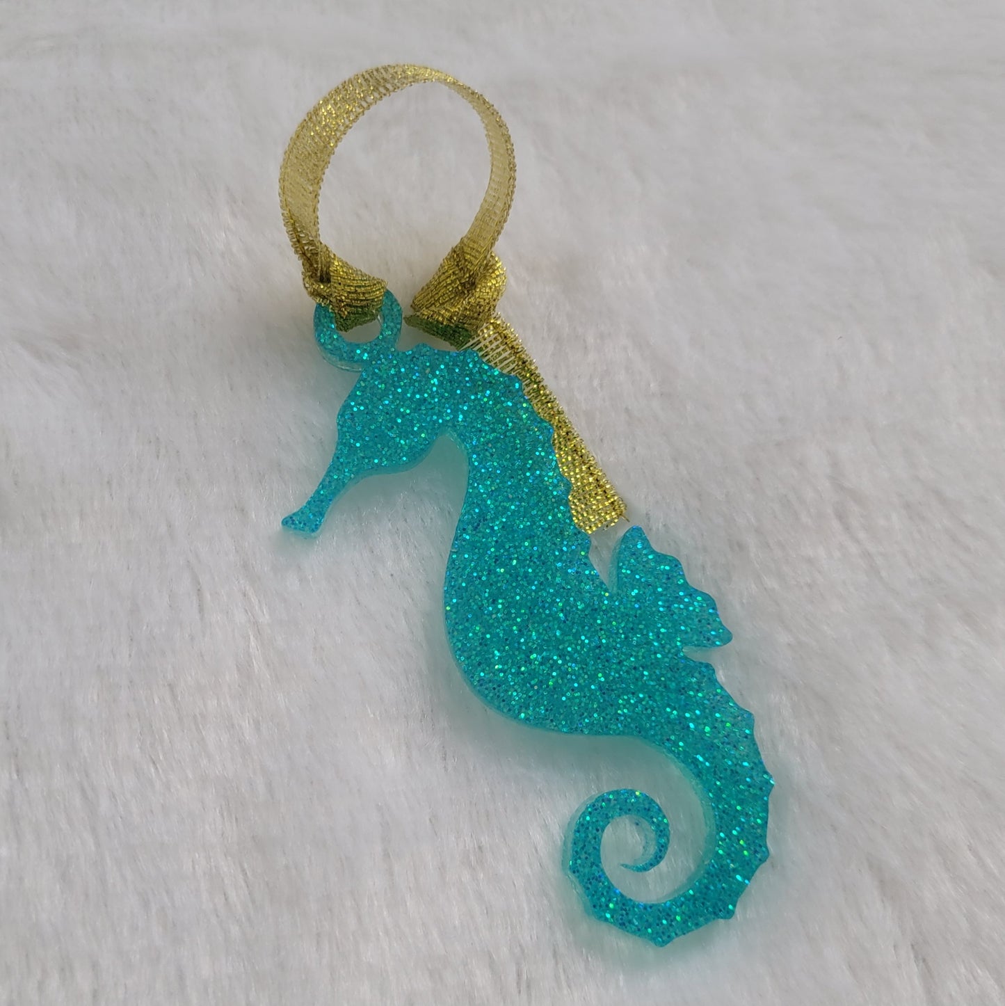 Seahorse shaped epoxy resin ornament, made with aqua glitter and a sparkling gold ribbon attached.