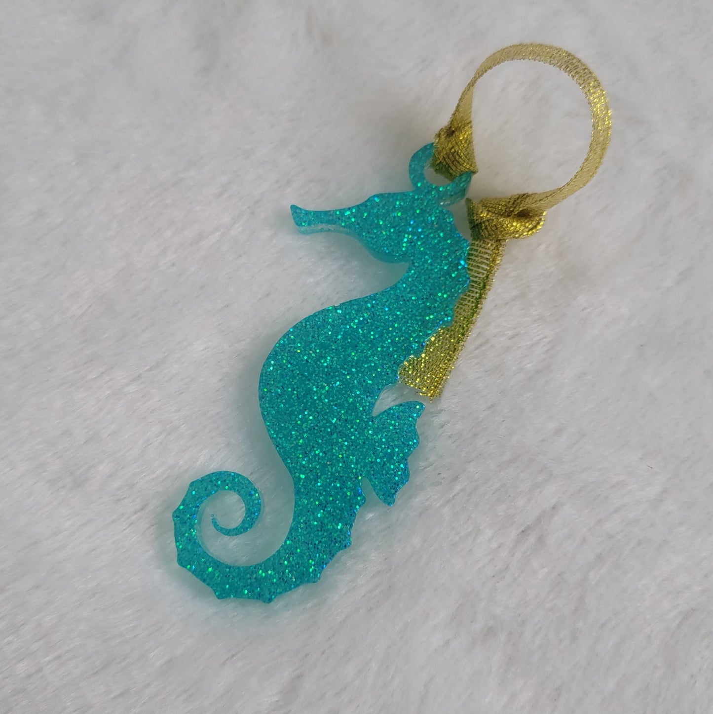 Seahorse shaped epoxy resin ornament, made with aqua glitter and a sparkling gold ribbon attached.