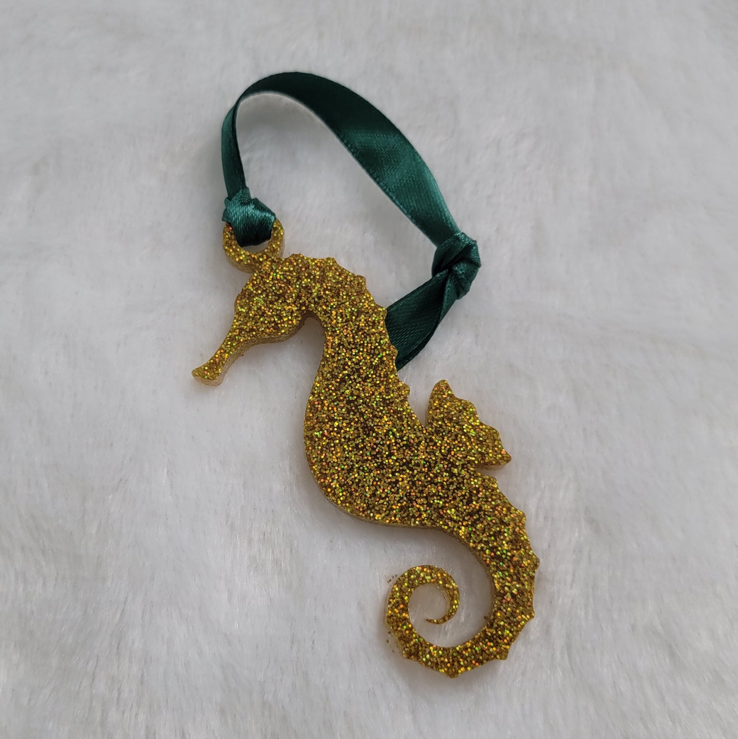 Seahorse shaped epoxy resin ornament, made with gold holographic glitter and a dark green ribbon attached.