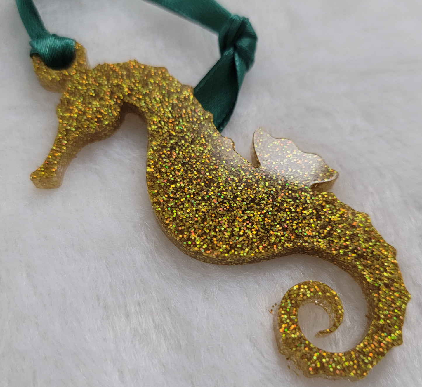 Seahorse shaped epoxy resin ornament, made with gold holographic glitter and a dark green ribbon attached.
