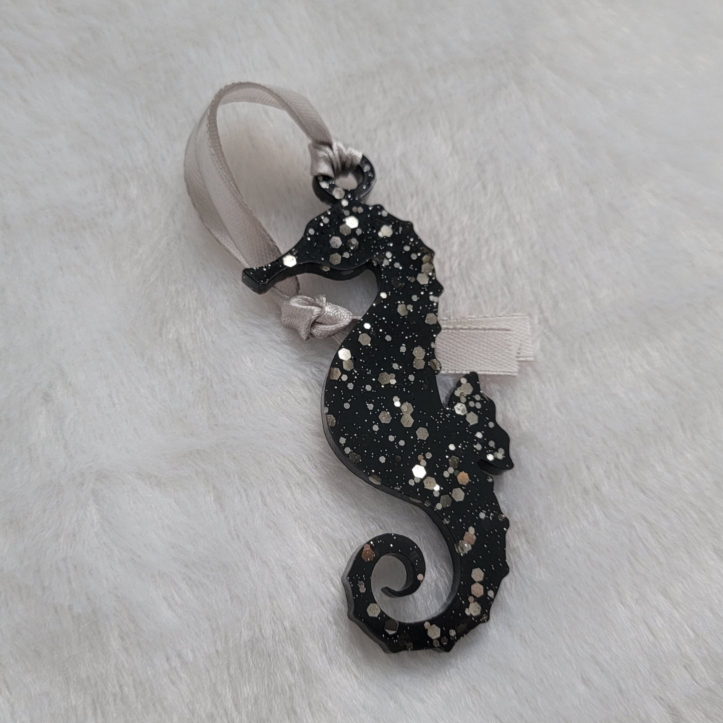 Seahorse shaped epoxy resin ornament, made with black pigment and warm silver glitter combined and a silver ribbon attached.