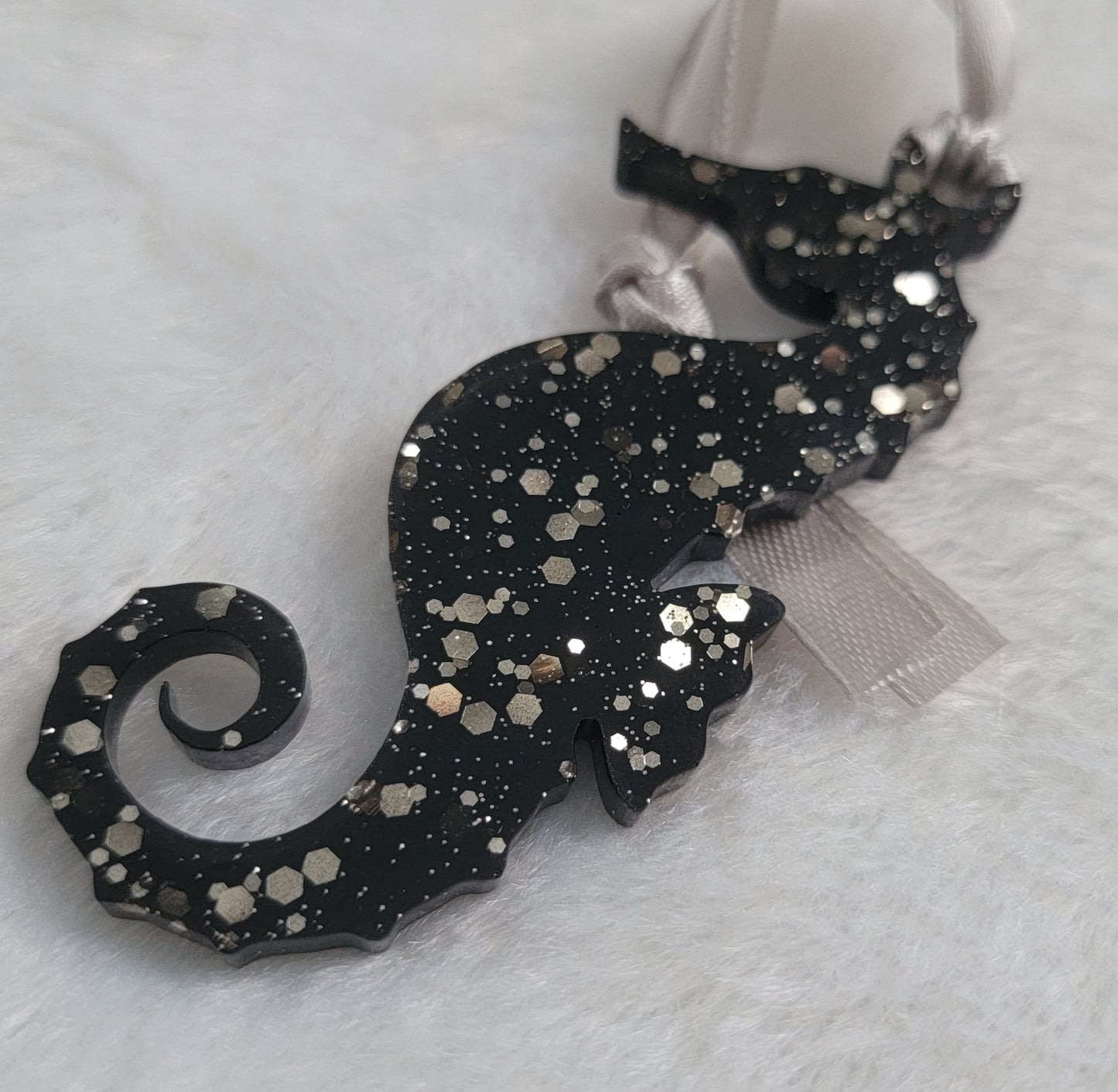 Seahorse shaped epoxy resin ornament, made with black pigment and warm silver glitter combined and a silver ribbon attached.