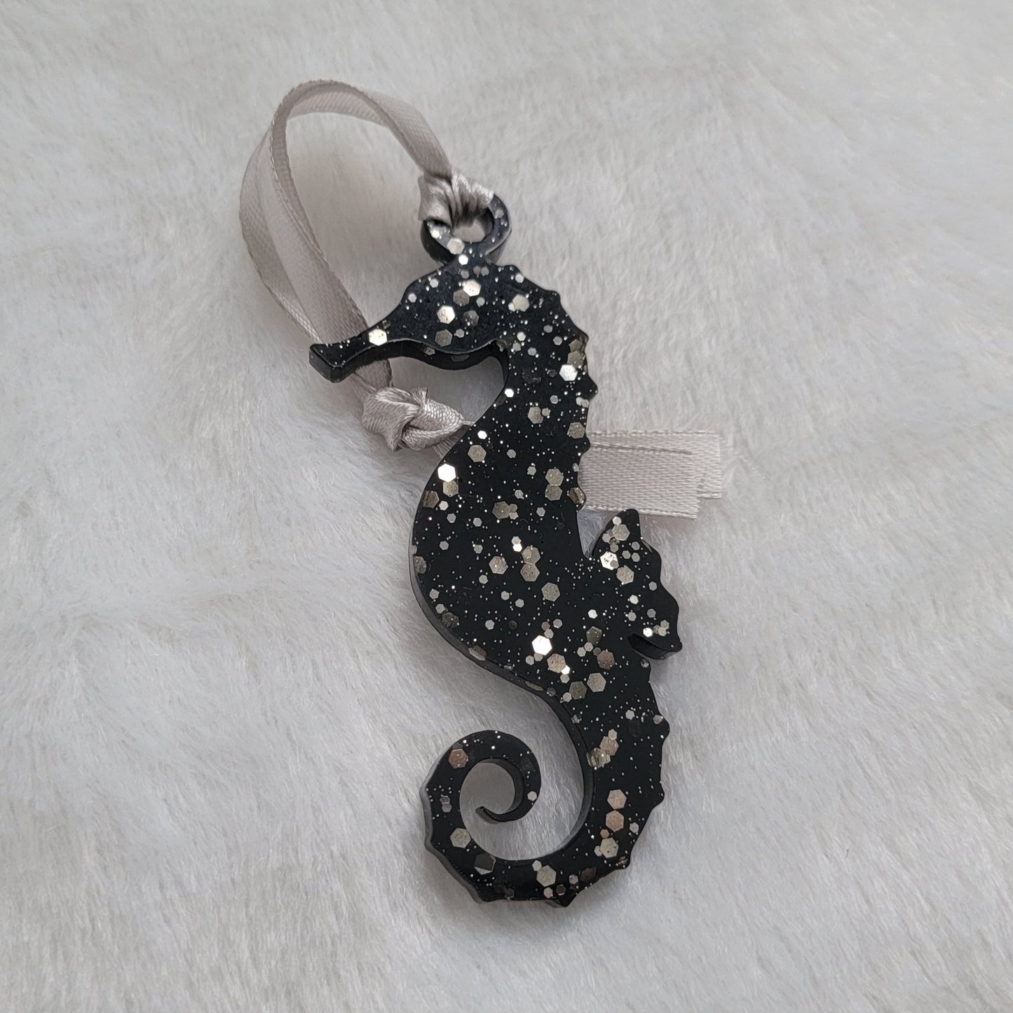 Seahorse shaped epoxy resin ornament, made with black pigment and warm silver glitter combined and a silver ribbon attached.