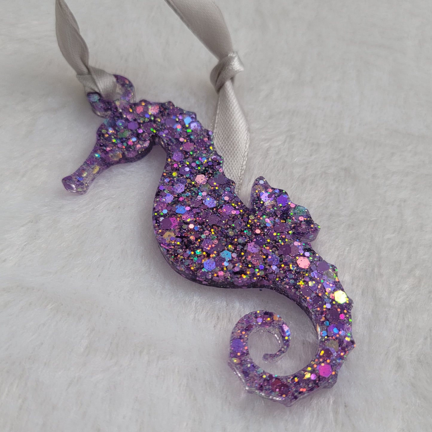 Seahorse shaped epoxy resin ornament, made with bright purple holographic glitter and a silver ribbon attached.