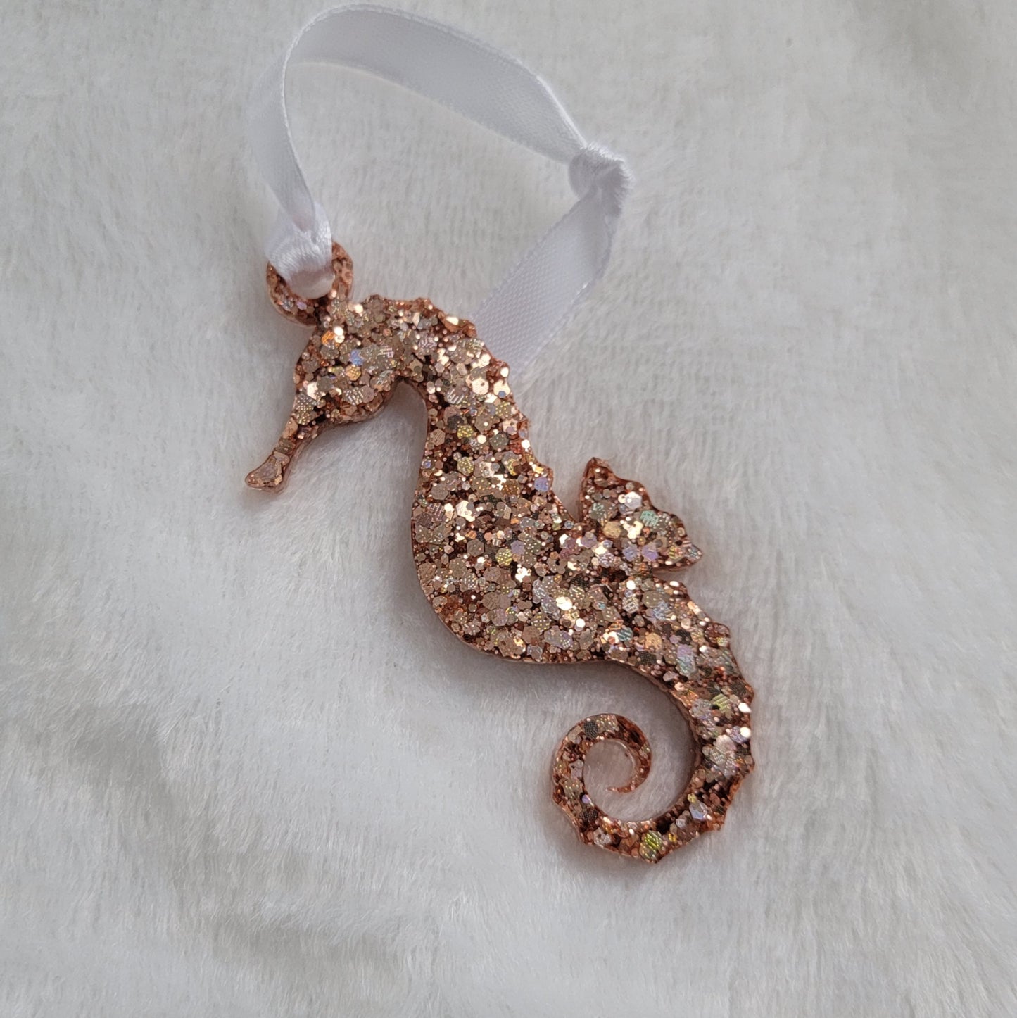 Seahorse shaped epoxy resin ornament, made with rose gold holographic glitter and a white ribbon attached.
