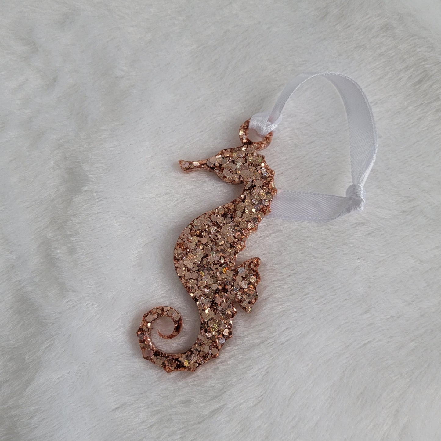 Seahorse shaped epoxy resin ornament, made with rose gold holographic glitter and a white ribbon attached.