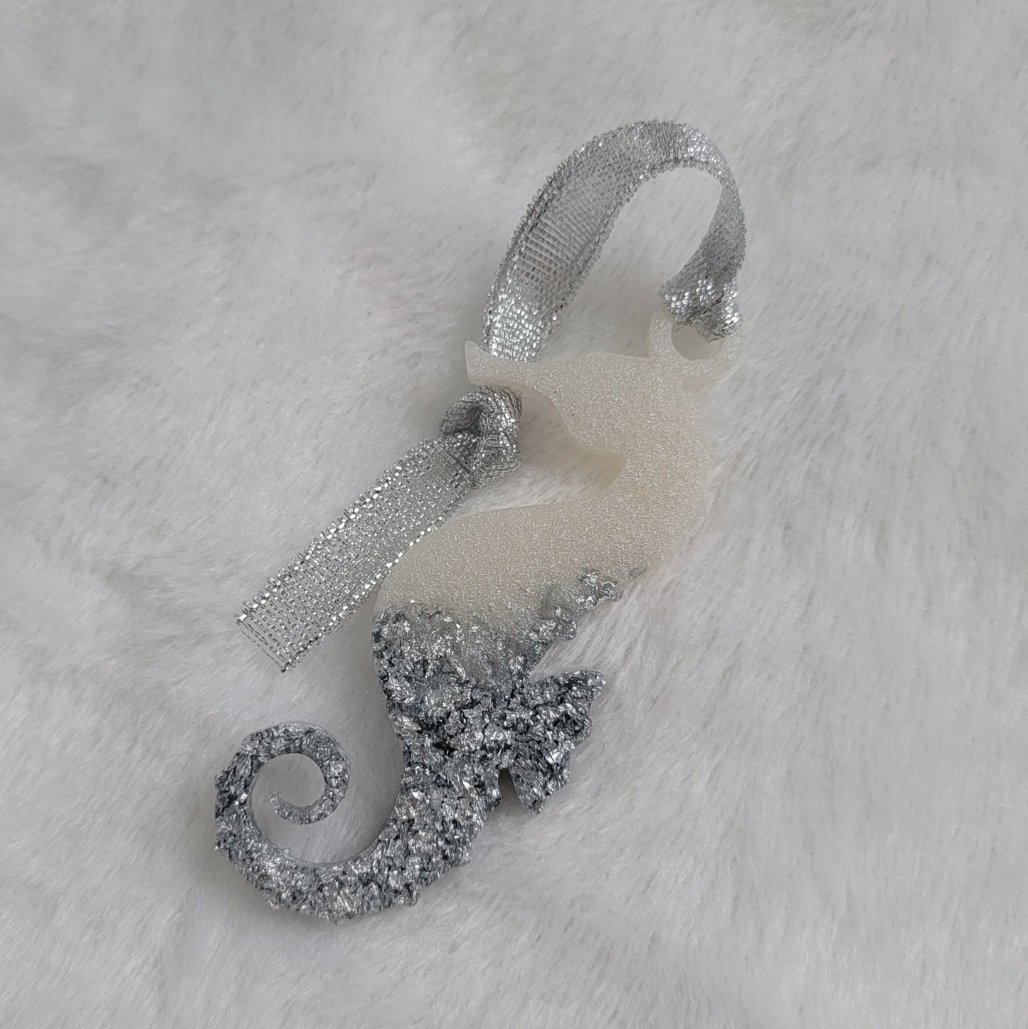 Seahorse shaped epoxy resin ornament, made with white pigment and silver foil flakes and a sparkling silver ribbon attached.