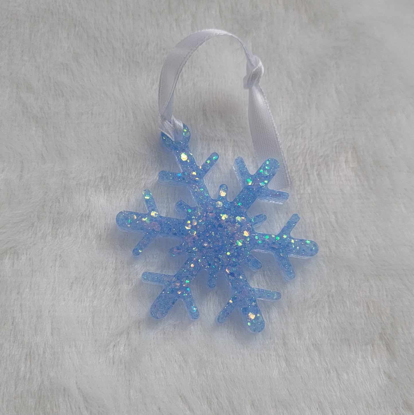 Snowflake shaped epoxy resin ornament, made with light blue iridescent glitter and a white ribbon attached.