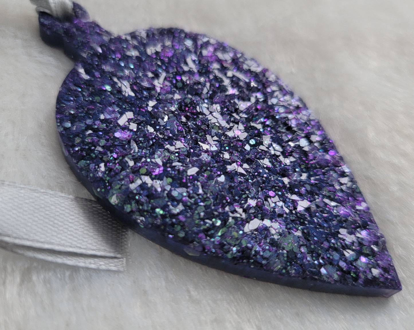 Drop shaped epoxy resin ornament that has a crystalline texture, made with purple and aqua blue holographic glitter and a silver ribbon attached.