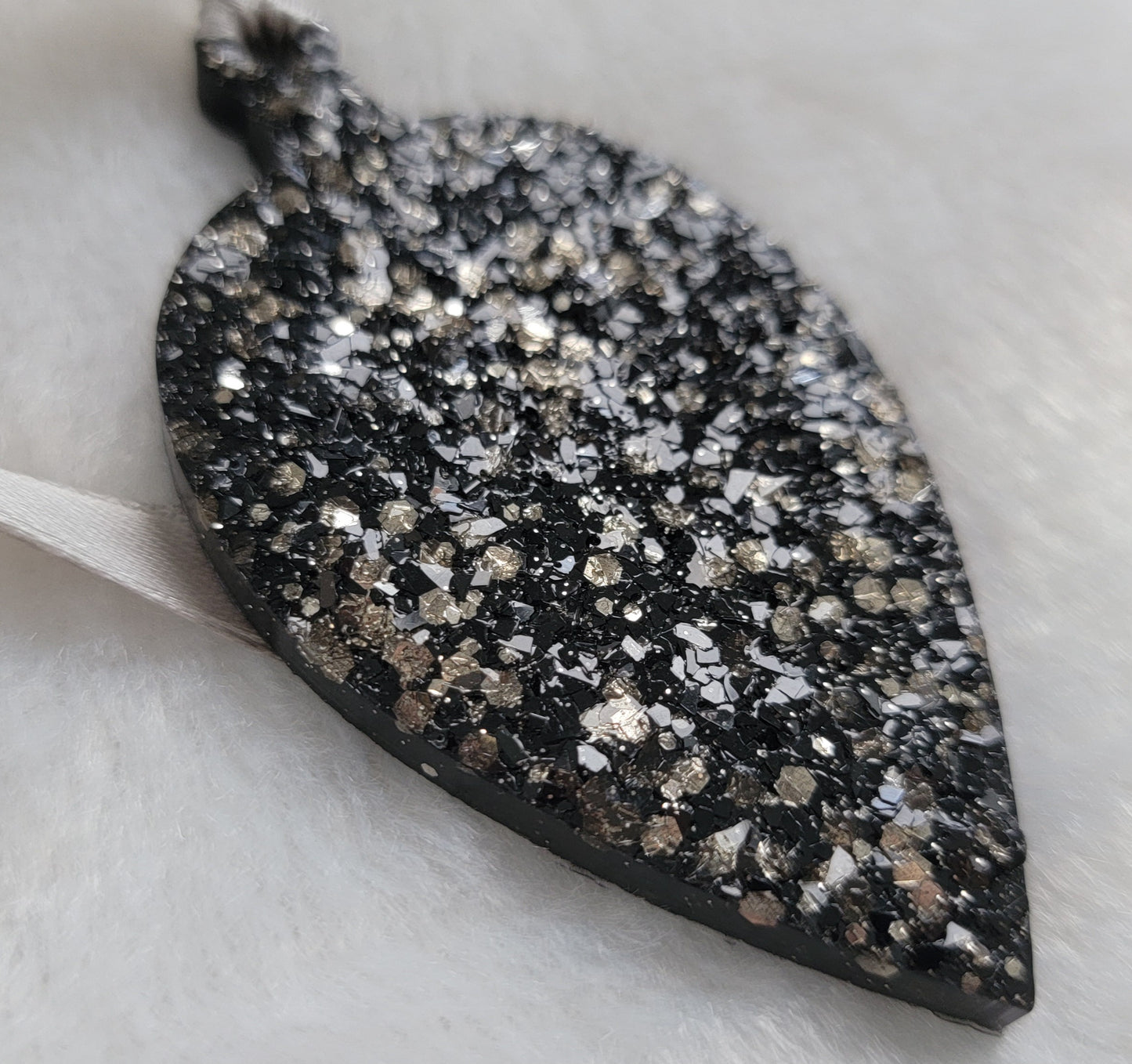 Drop shaped epoxy resin ornament that has a crystalline texture, made with black pigment and warm silver glitter combined and a silver ribbon attached.