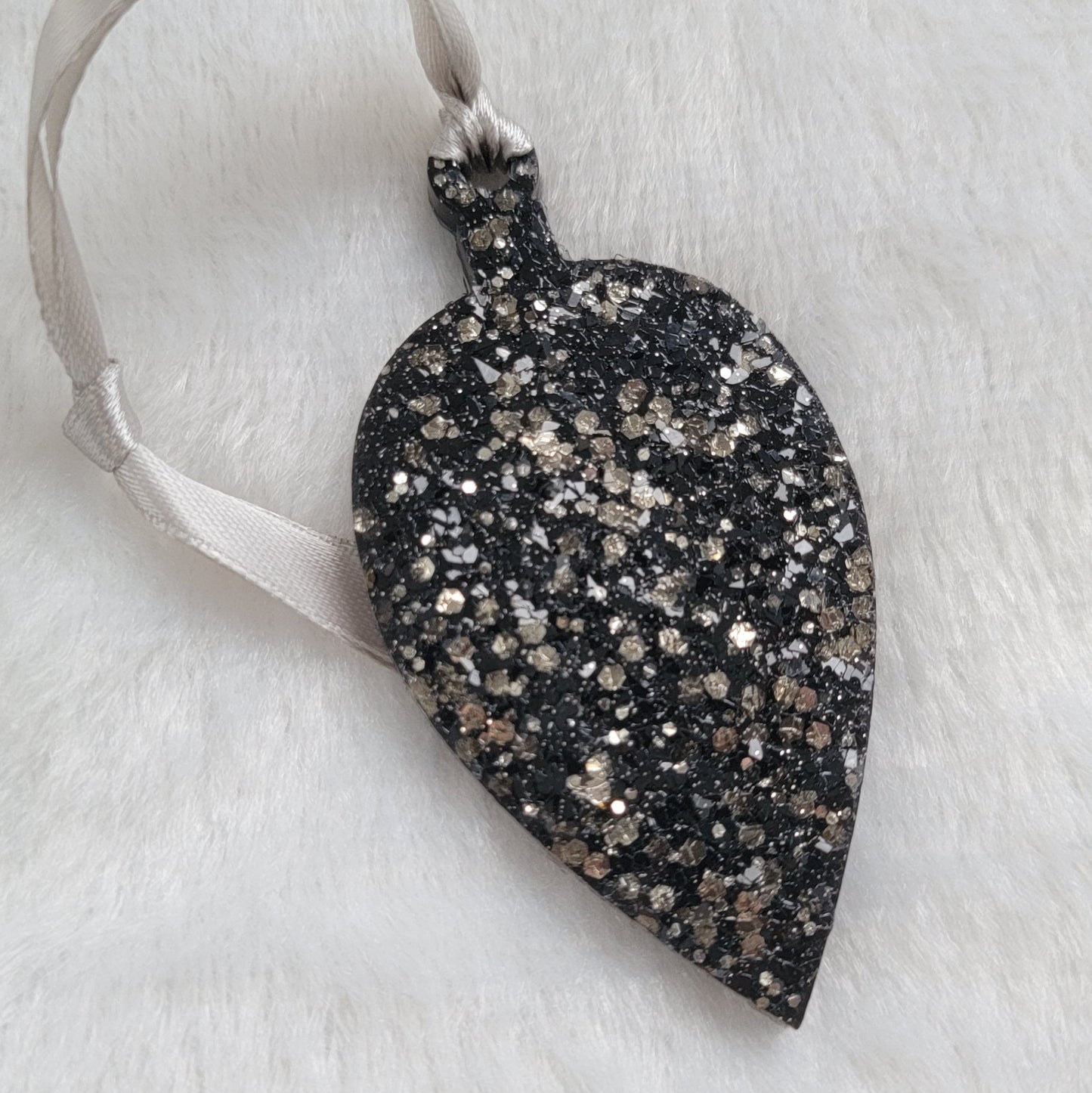 Drop shaped epoxy resin ornament that has a crystalline texture, made with black pigment and warm silver glitter combined and a silver ribbon attached.