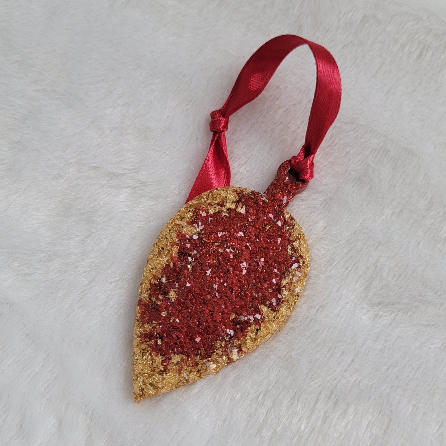 Drop shaped epoxy resin ornament that has a crystalline texture, made with gold foil flakes and cherry red pigment and a red ribbon attached.