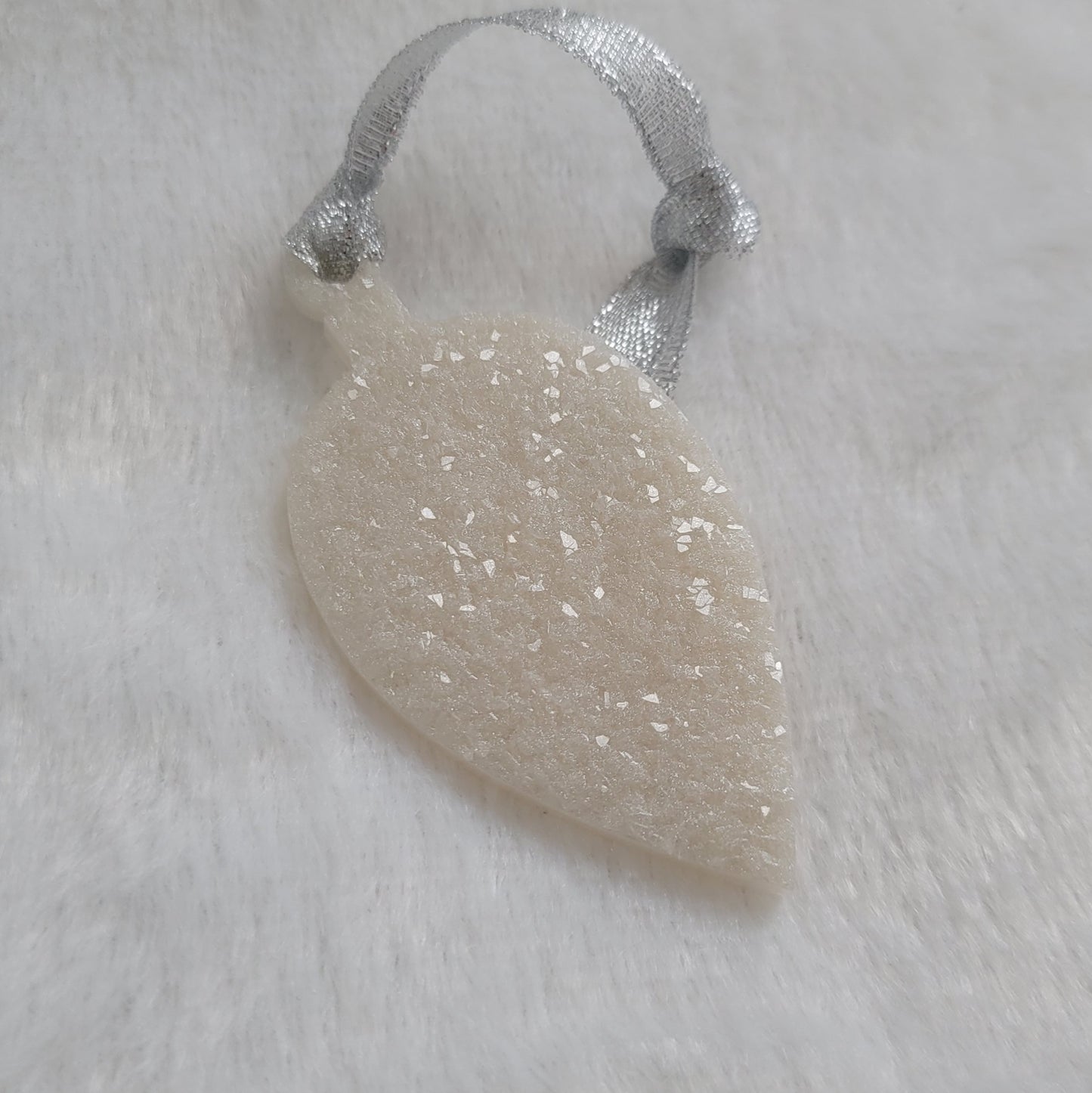 Drop shaped epoxy resin ornament that has a crystalline texture, made with white pigment and a sparkling silver ribbon attached.