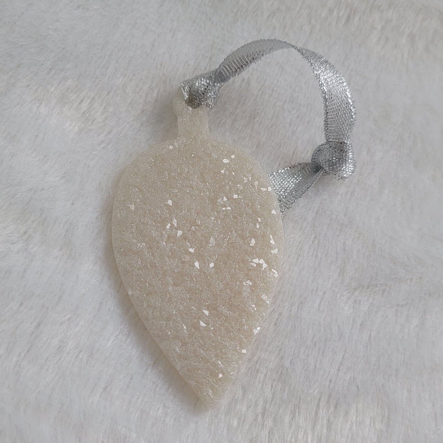 Drop shaped epoxy resin ornament that has a crystalline texture, made with white pigment and a sparkling silver ribbon attached.