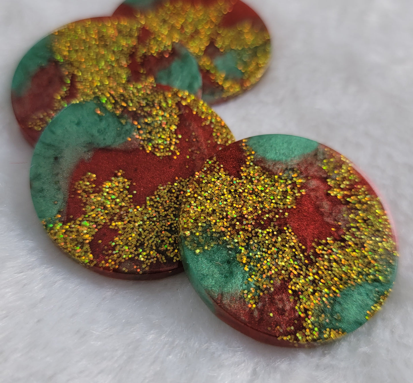Four round epoxy resin pieces with swirled red and green pigment and gold holographic glitter.