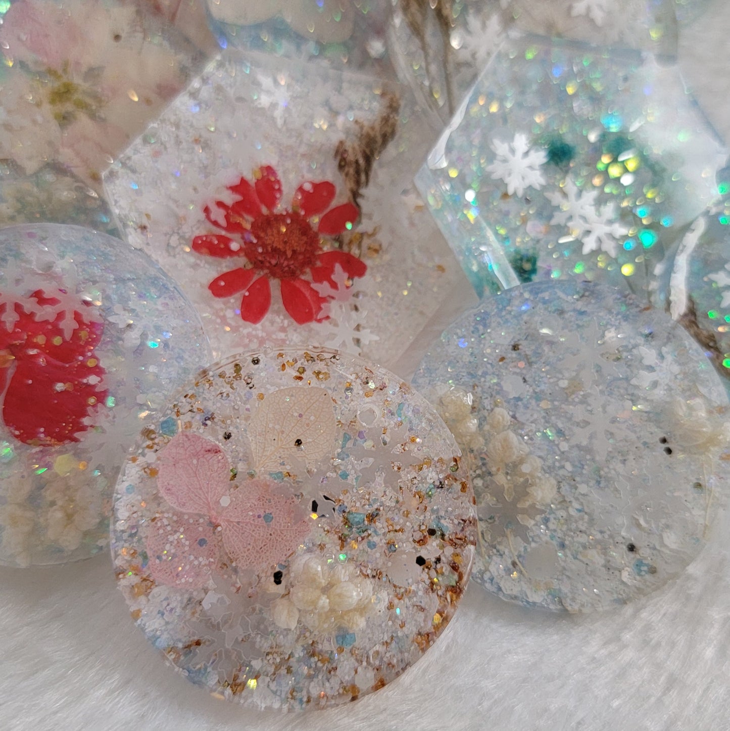 Array of round a hexagon shaped glittery epoxy resin pieces that contain snowflake glitters and pressed flowers.