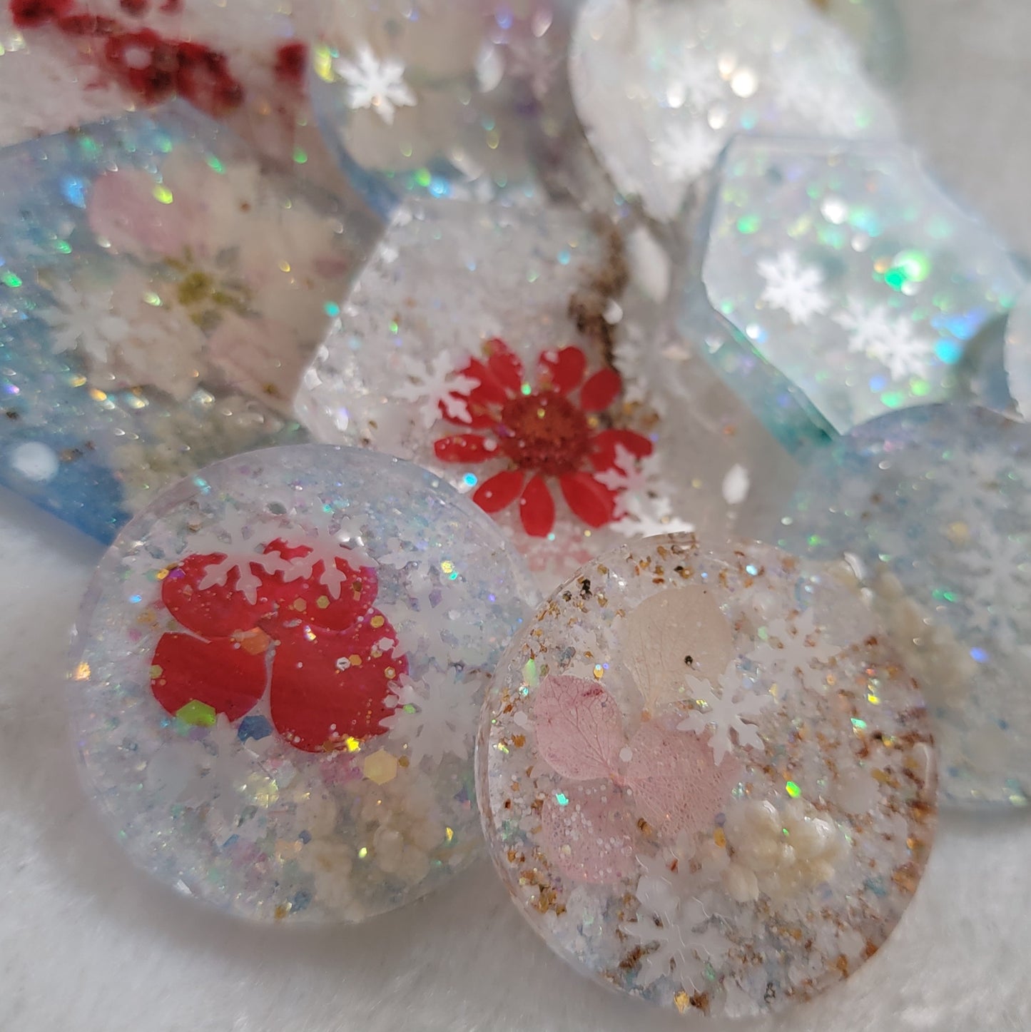 Array of various light glittery epoxy resin pieces that contain snowflake glitters and pressed flowers.