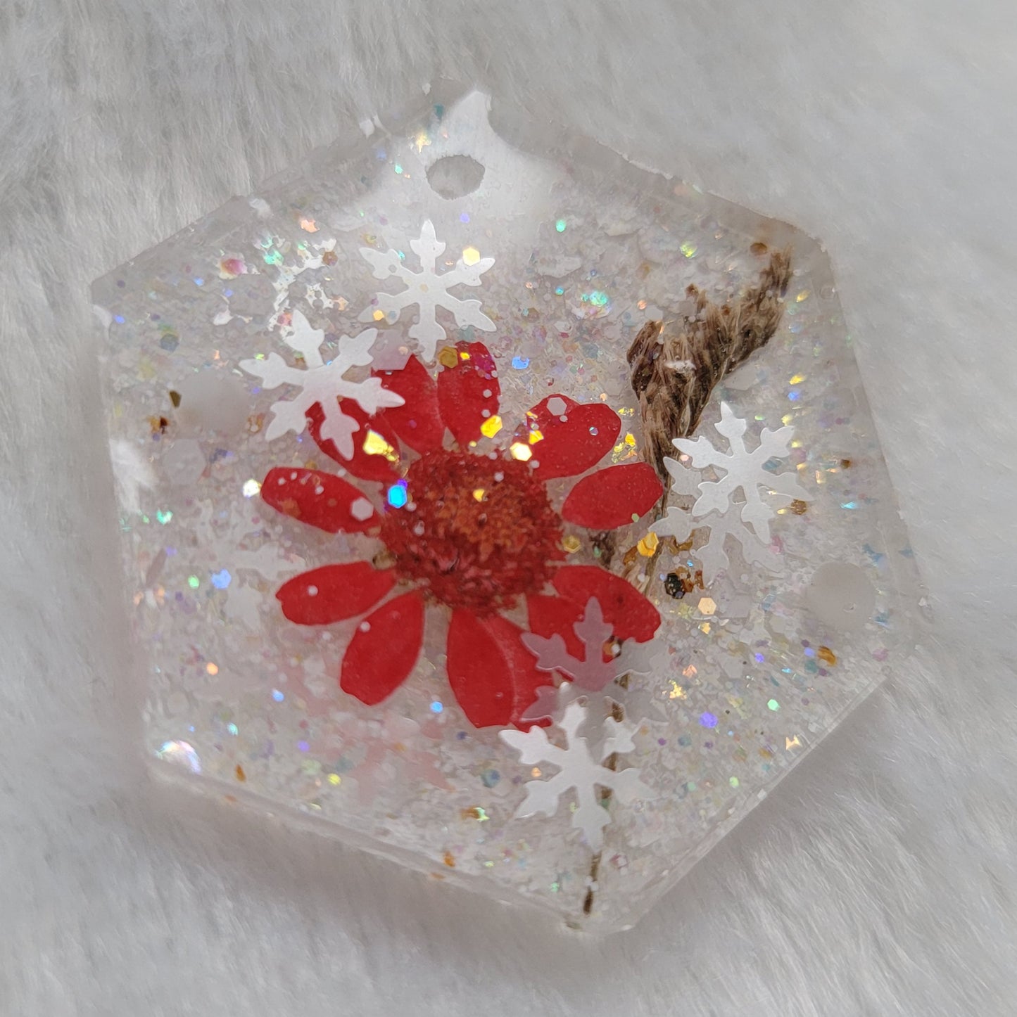 Glittery hexagon shaped epoxy resin piece containing snowflake glitters and a red daisy and brown grass blossom stalks.