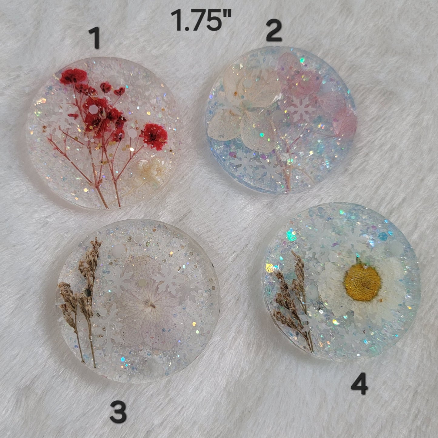 Four round glittery epoxy resin pieces that contain snowflake glitters and pressed flowers.