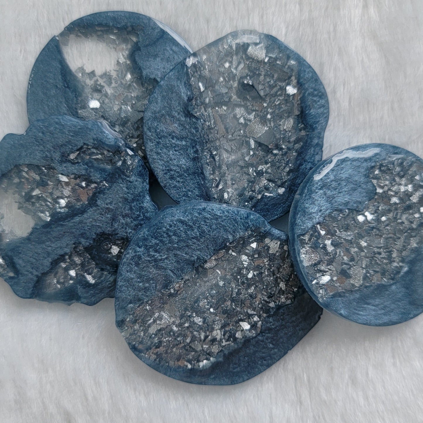 Five round and irregular round epoxy resin pieces made with ice blue mica pigment and silver crystalline texture insets.