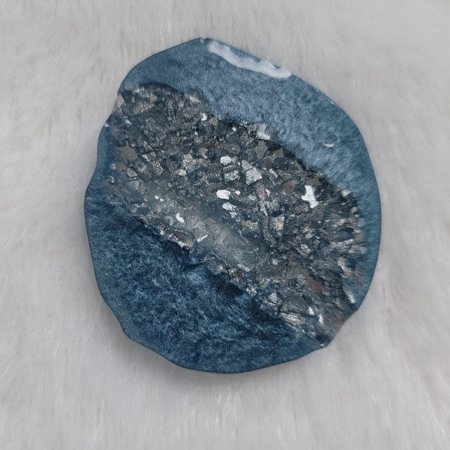 Irregular round epoxy resin piece made with ice blue mica pigment and silver crystalline texture inset running through the center of the piece.