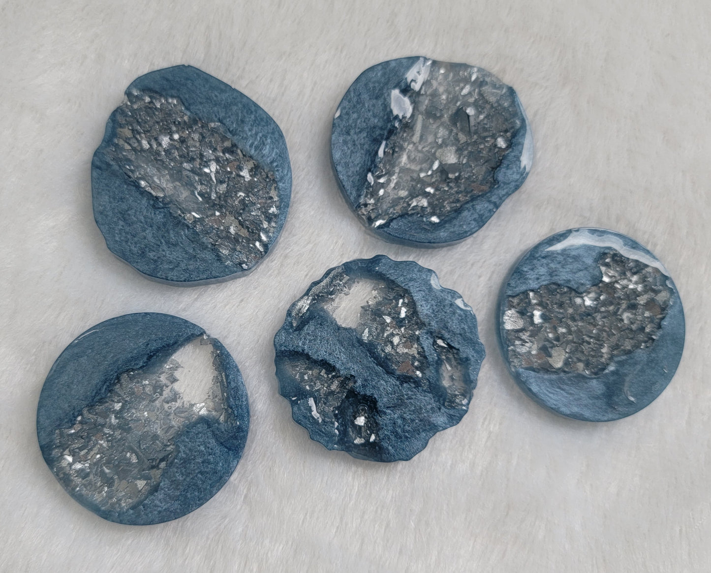 Five round and irregular round epoxy resin pieces made with ice blue mica pigment and silver crystalline texture insets.