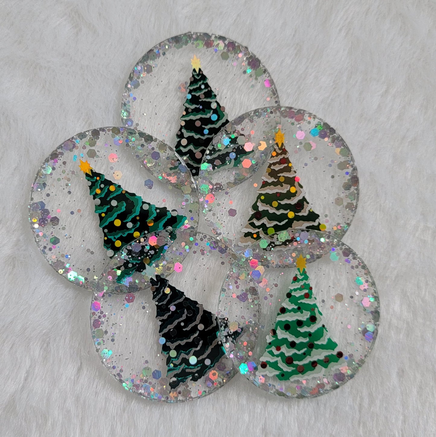 Five round epoxy resin pieces with silver holographic glitter and vinyl Christmas tree designs on them.