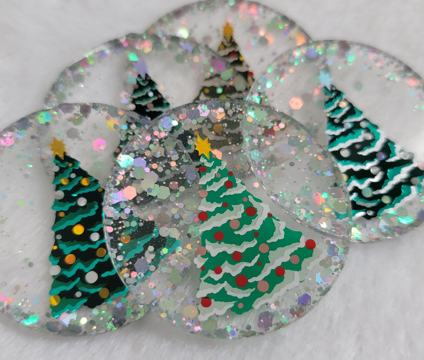 Five round epoxy resin pieces with silver holographic glitter and vinyl Christmas tree designs on them.
