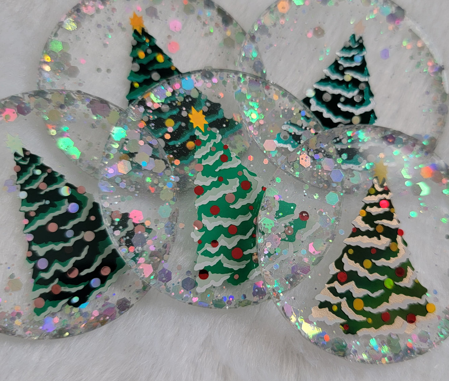 Five round epoxy resin pieces with silver holographic glitter and vinyl Christmas tree designs on them.