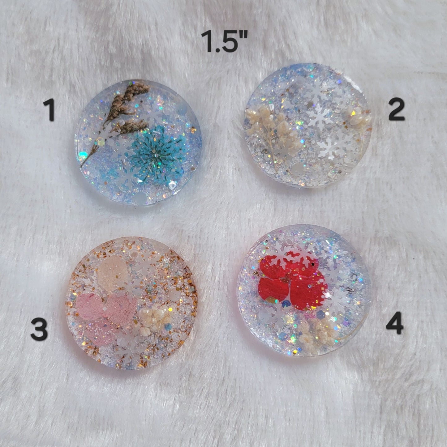 Four round glittery epoxy resin pieces that contain snowflake glitters and pressed flowers.