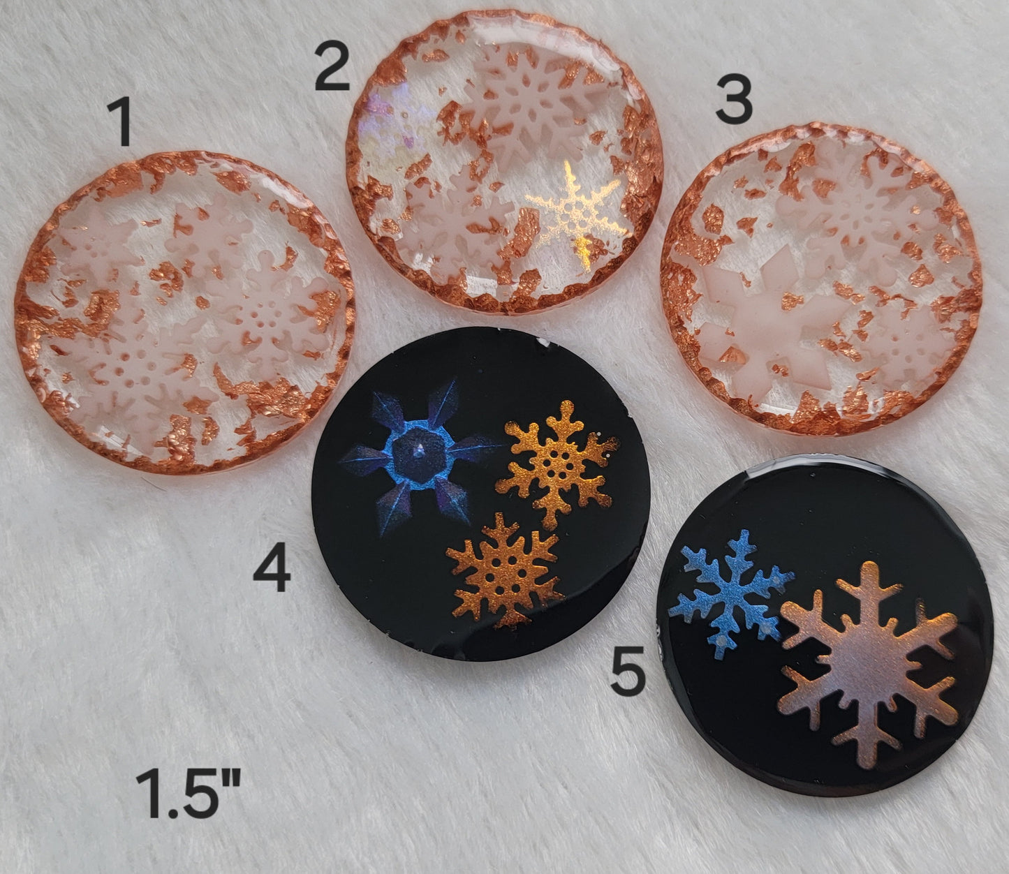 Five round epoxy resin pieces, two with iridescent resin snowflakes and black backgrounds and three with white snowflakes and copper accents.